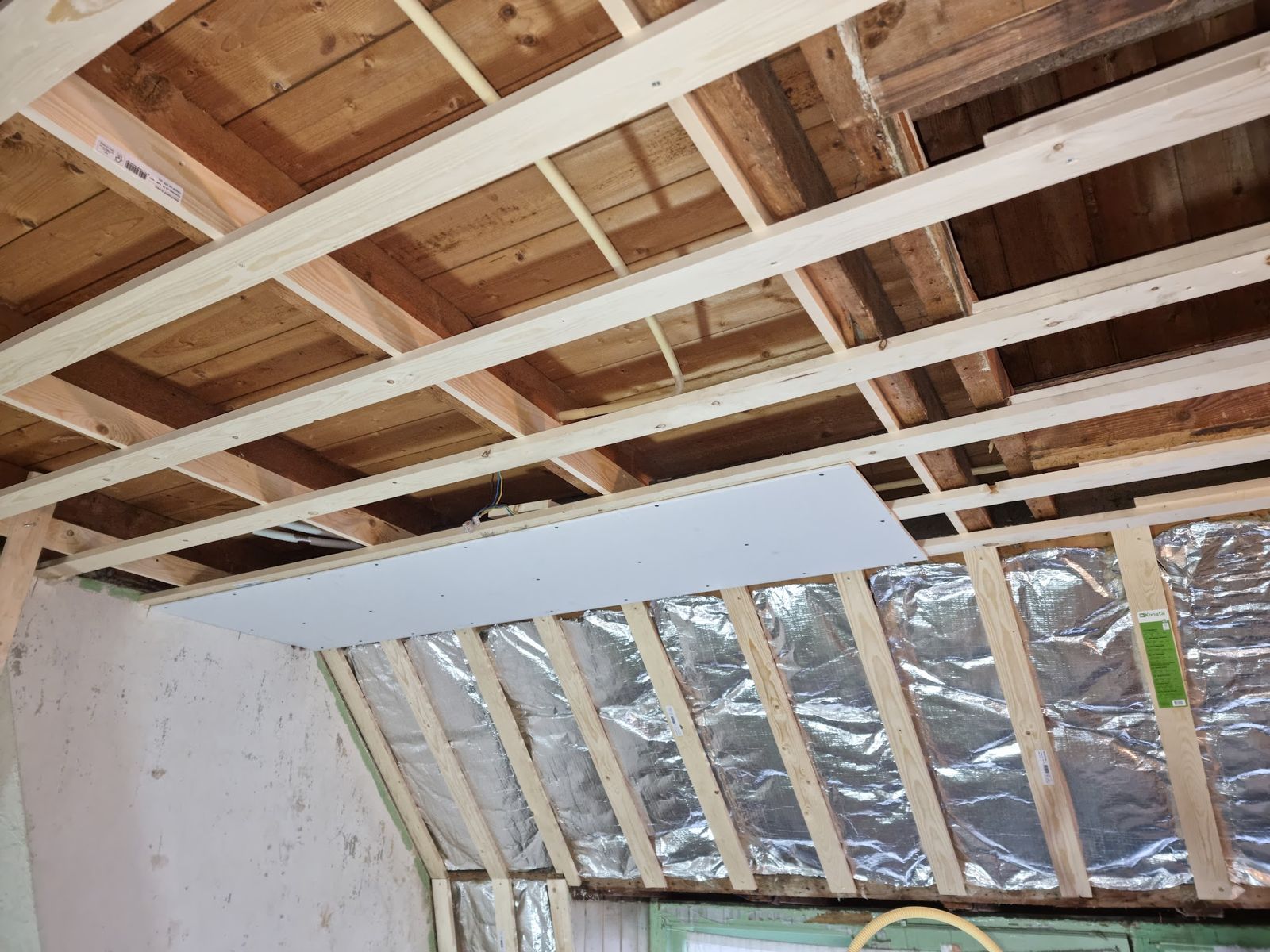 Nieuw houten regelwerk onder het dak met reflecterende isolatiefolie en de eerste gipsplaat