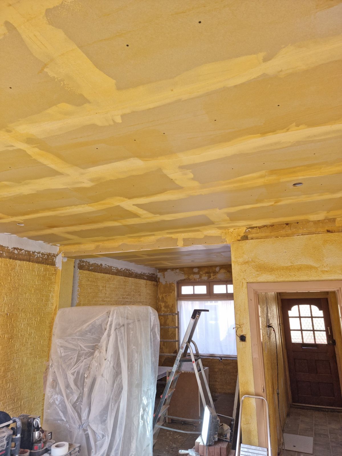 Gespoten isolatieschuim op plafond en wanden, meubels ingepakt in folie