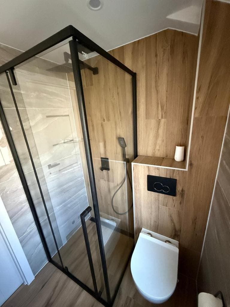 Douche met zwart omlijst glas naast een wand van houtlook tegels