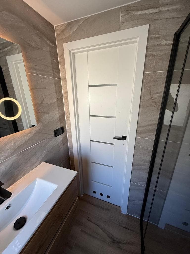 Getegelde badkamer met witte binnendeur en een verlichte ronde spiegel